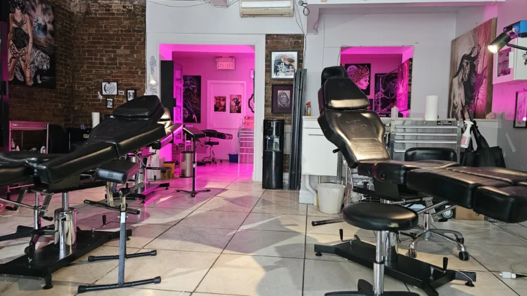 Interior of Tattoo Abyss Montreal studio featuring black adjustable tattoo chairs, brick walls, framed artwork, and pink ambient lighting in a clean professional workspace.